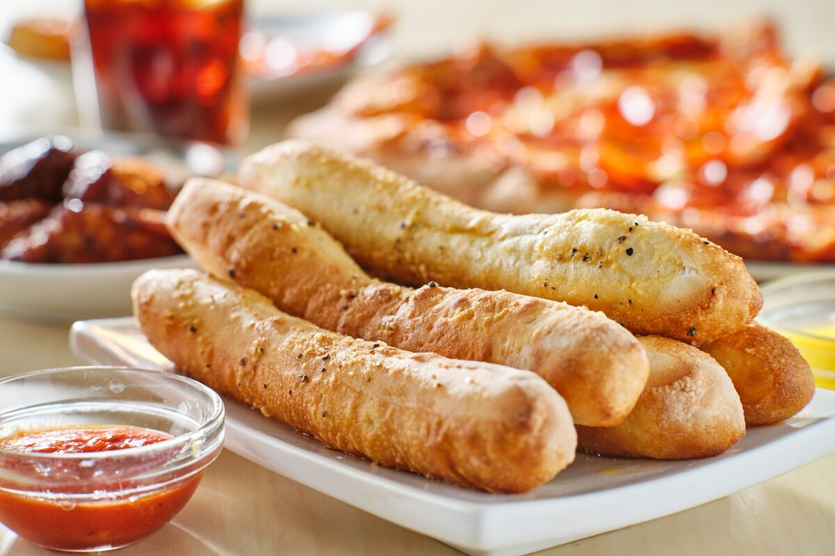 garlic butter breadsticks with soda and pizza in background