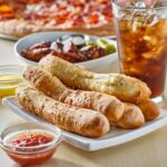 garlic butter breadsticks with soda and pizza in background