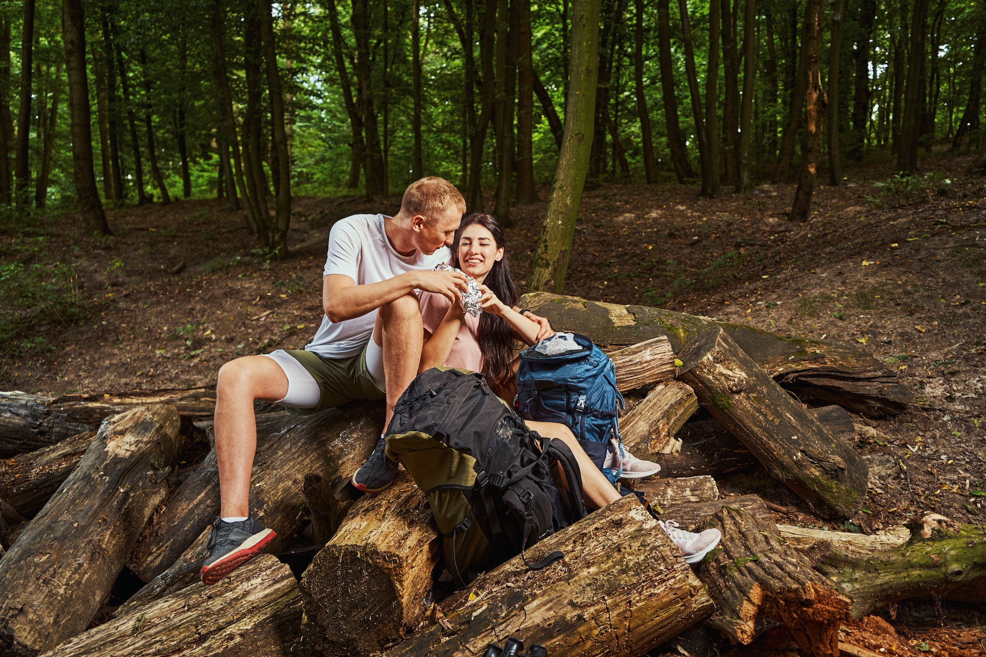 Smiling couple eating snacks while hiking in forest